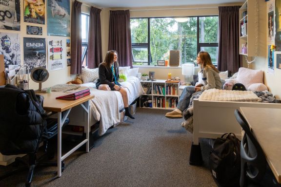 Two girls in a sunnydorm room talking by the window