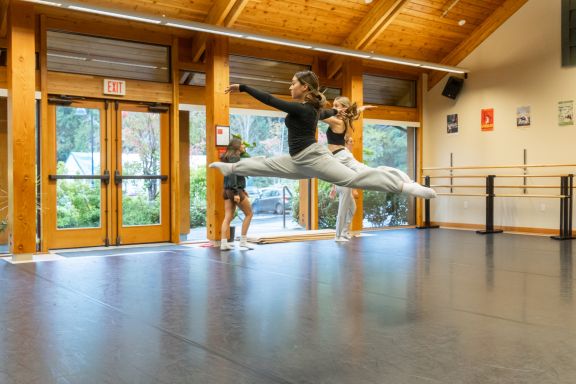 Dance students practicing a synchronized leap in sunlit studio