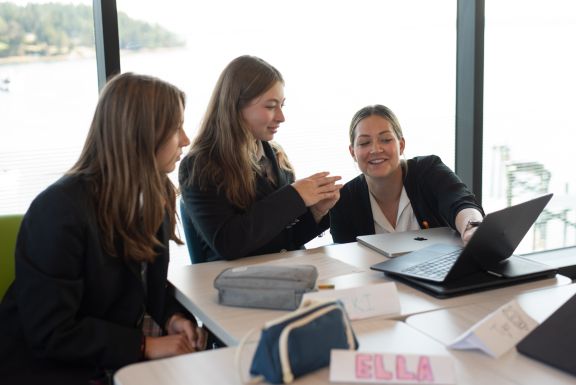 Teacher crouches down to help students at their desk with ocean view behind