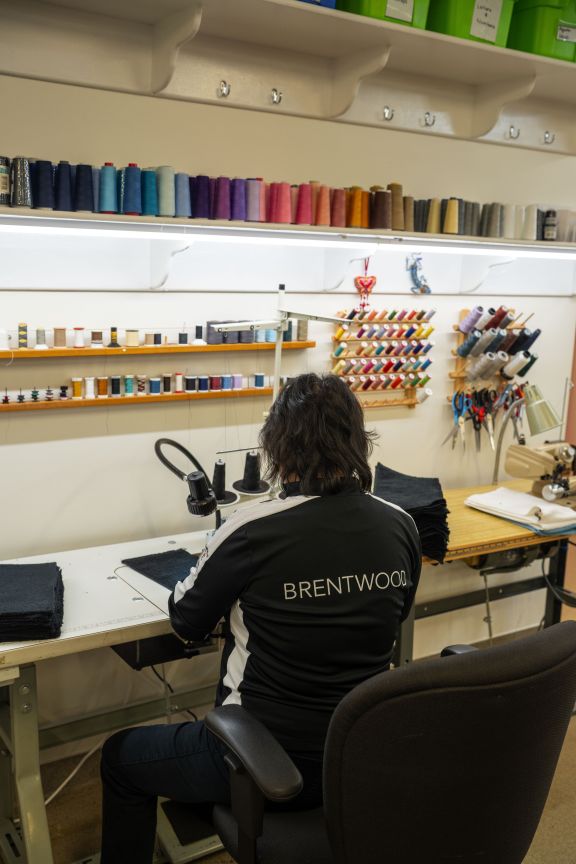 Laundry Services team member tailors and repairs student uniforms with colourful spools of thread in front of her